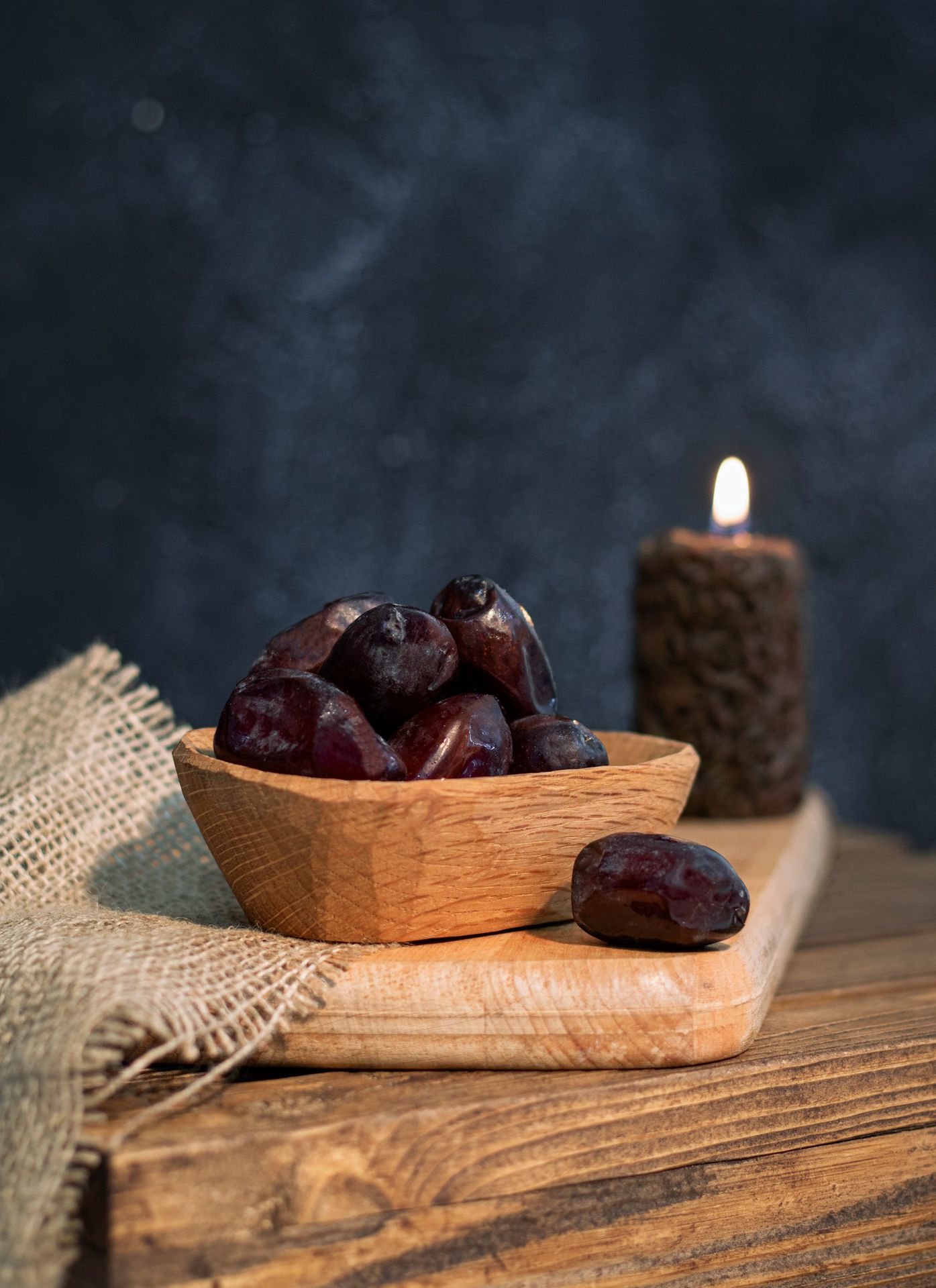 a wooden bowl filled with plums next to a lit candle